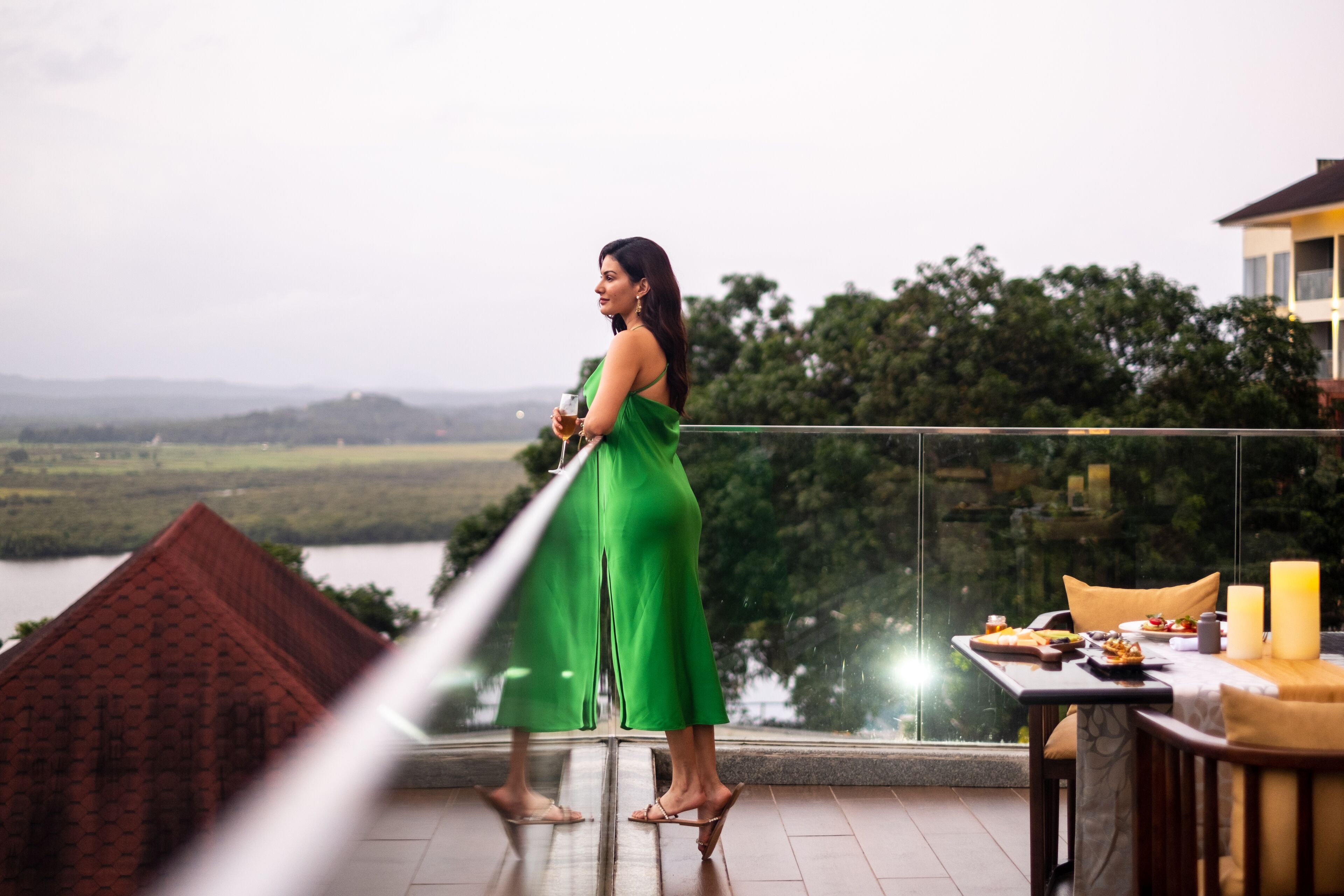 Eine Frau in einem grünen Kleid steht auf einem Balkon und blickt auf eine reizvolle Landschaft mit einem Essplatz.