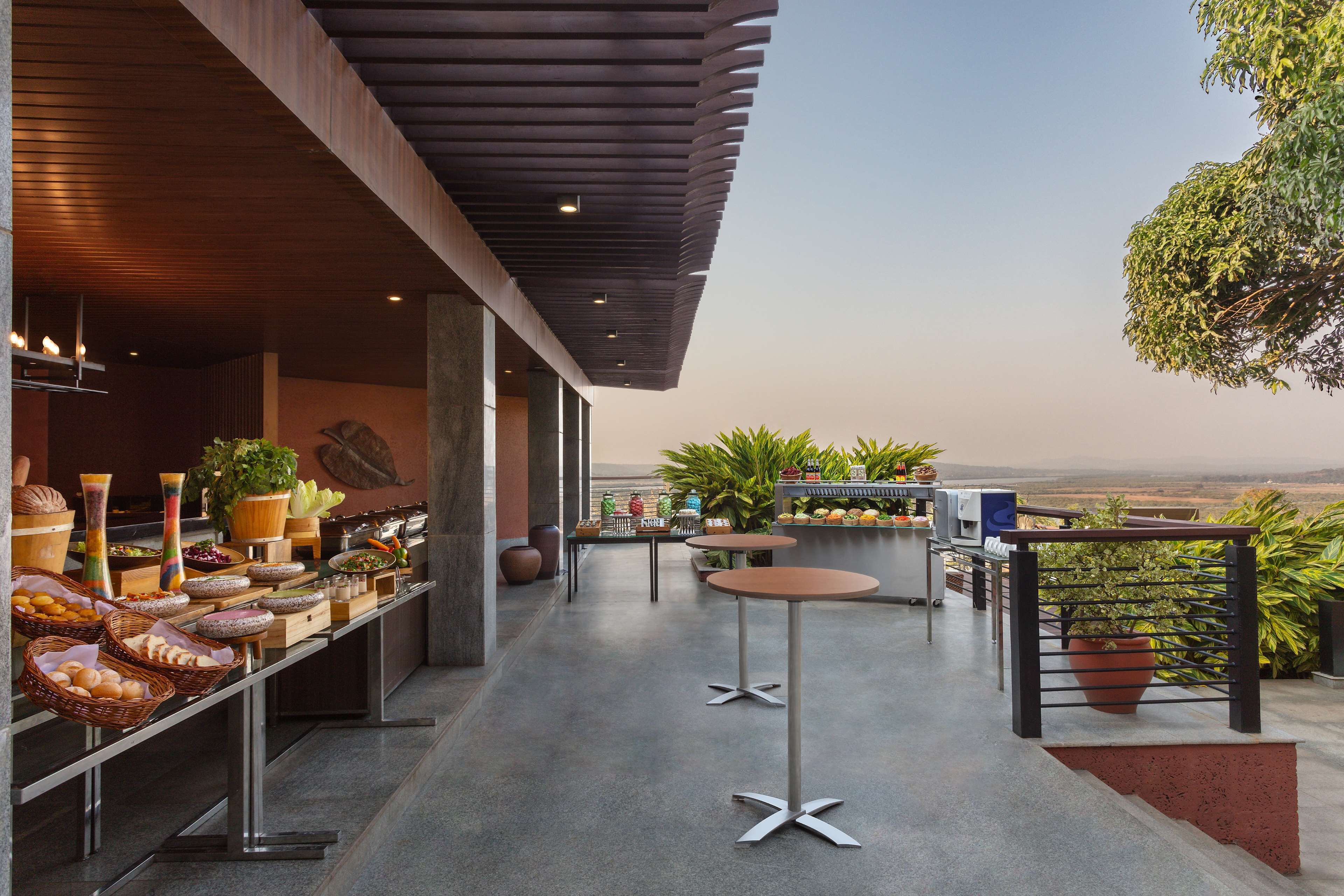 A modern outdoor dining area with a long counter, multiple tables, and potted plants.