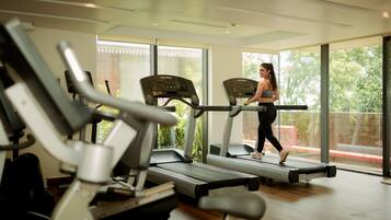 Un gimnasio con cintas de correr y equipamiento de ejercicio, ventanas amplias y vistas a zonas verdes.