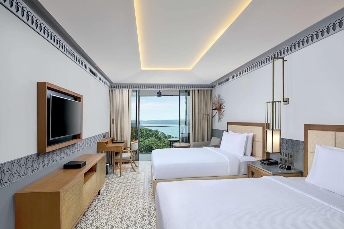 Habitación de hotel con dos camas, televisión, escritorio y vistas al exterior.