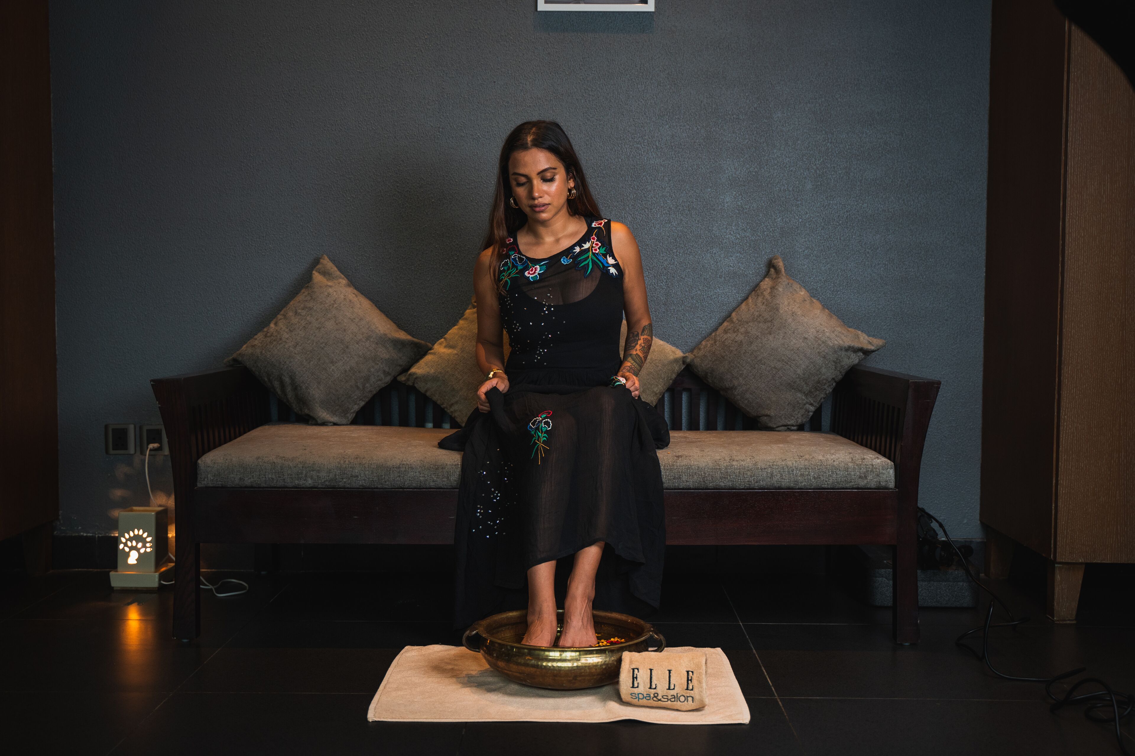 A woman standing on a platform with a bowl in front of a sofa and a sign that reads "ELLE spa & salon".