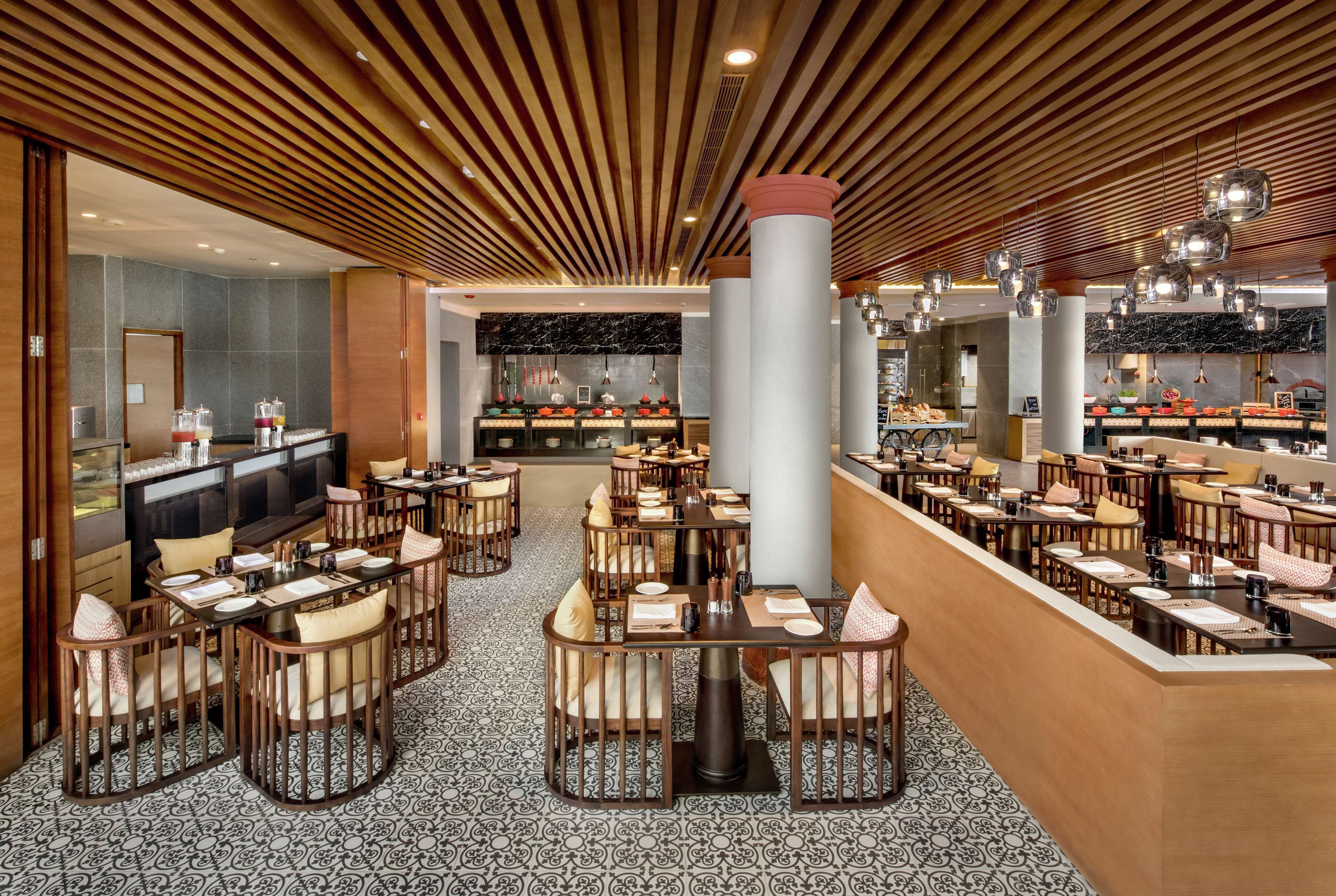 Een ruim restaurant met verschillende eetgedeeltes, een houten plafond en vloertegels met een patroon.