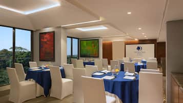 Uma sala de conferências com mesas montadas para uma reunião, grandes janelas com vista para o exterior e uma placa indicando que o espaço pertence ao hotel DoubleTree by Hilton.