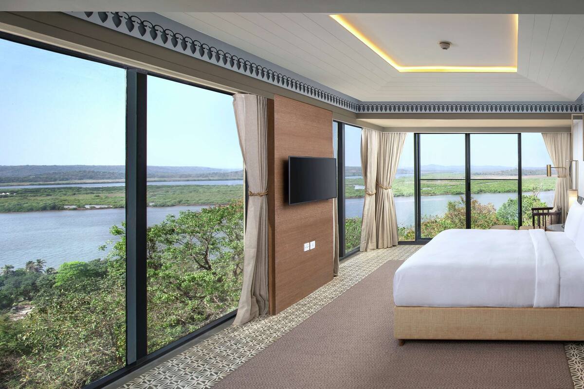Habitación de hotel con una cama grande, televisión y vista a un río y vegetación.
