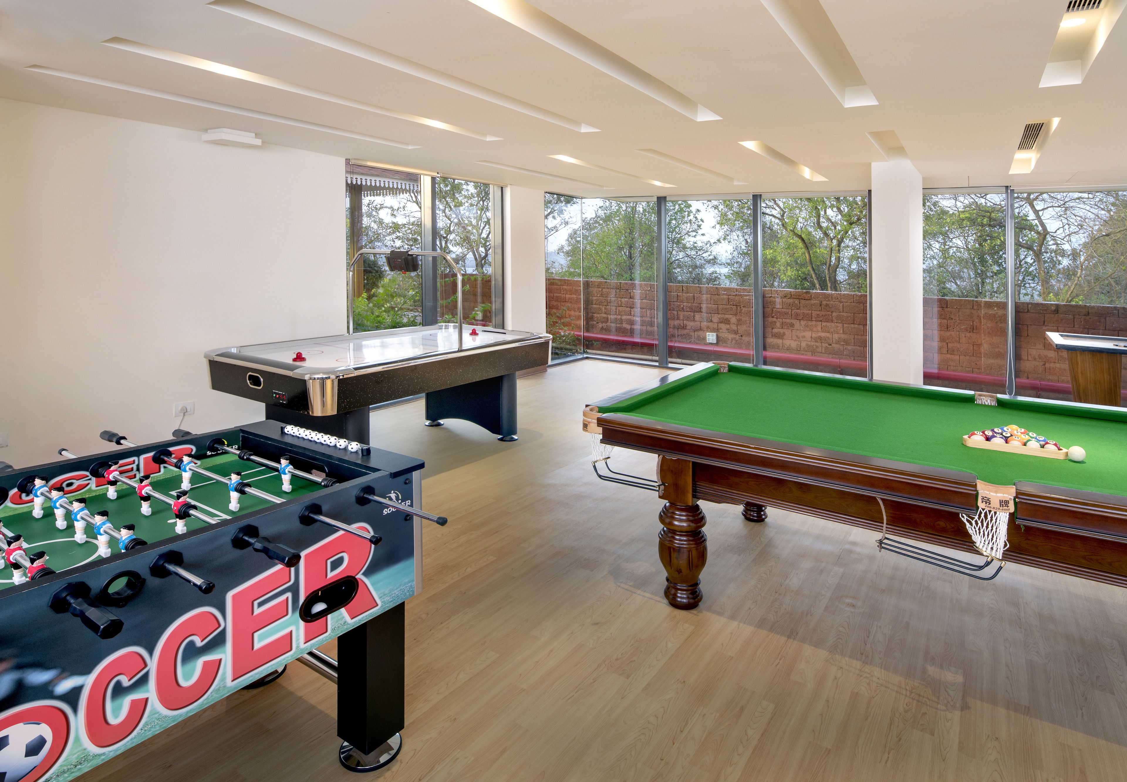 Une table de billard et une table de baby-foot dans une pièce bien éclairée, dotée de grandes fenêtres.