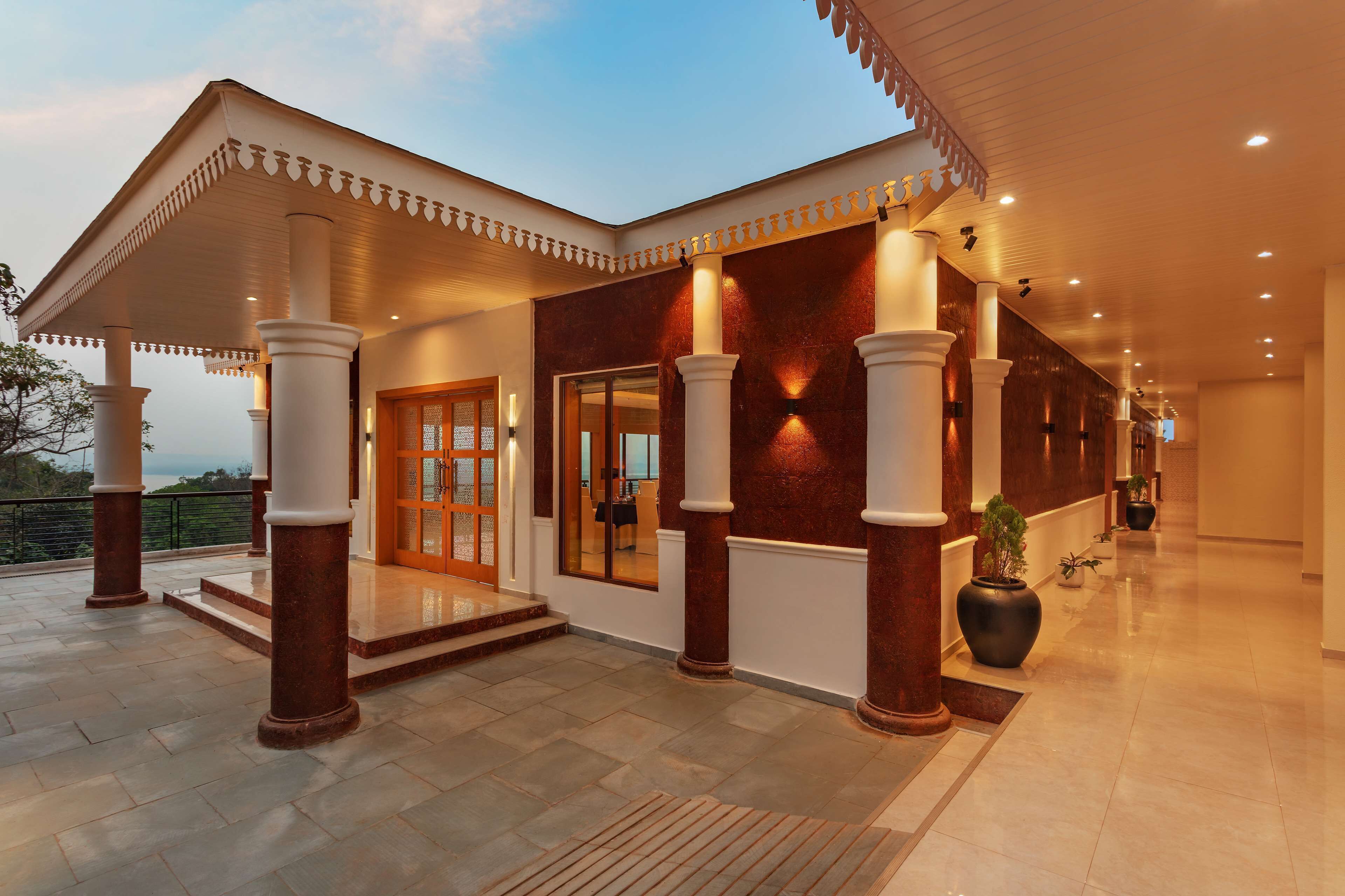 Entrada de hotel con un porche cubierto, columnas y una planta grande en maceta.