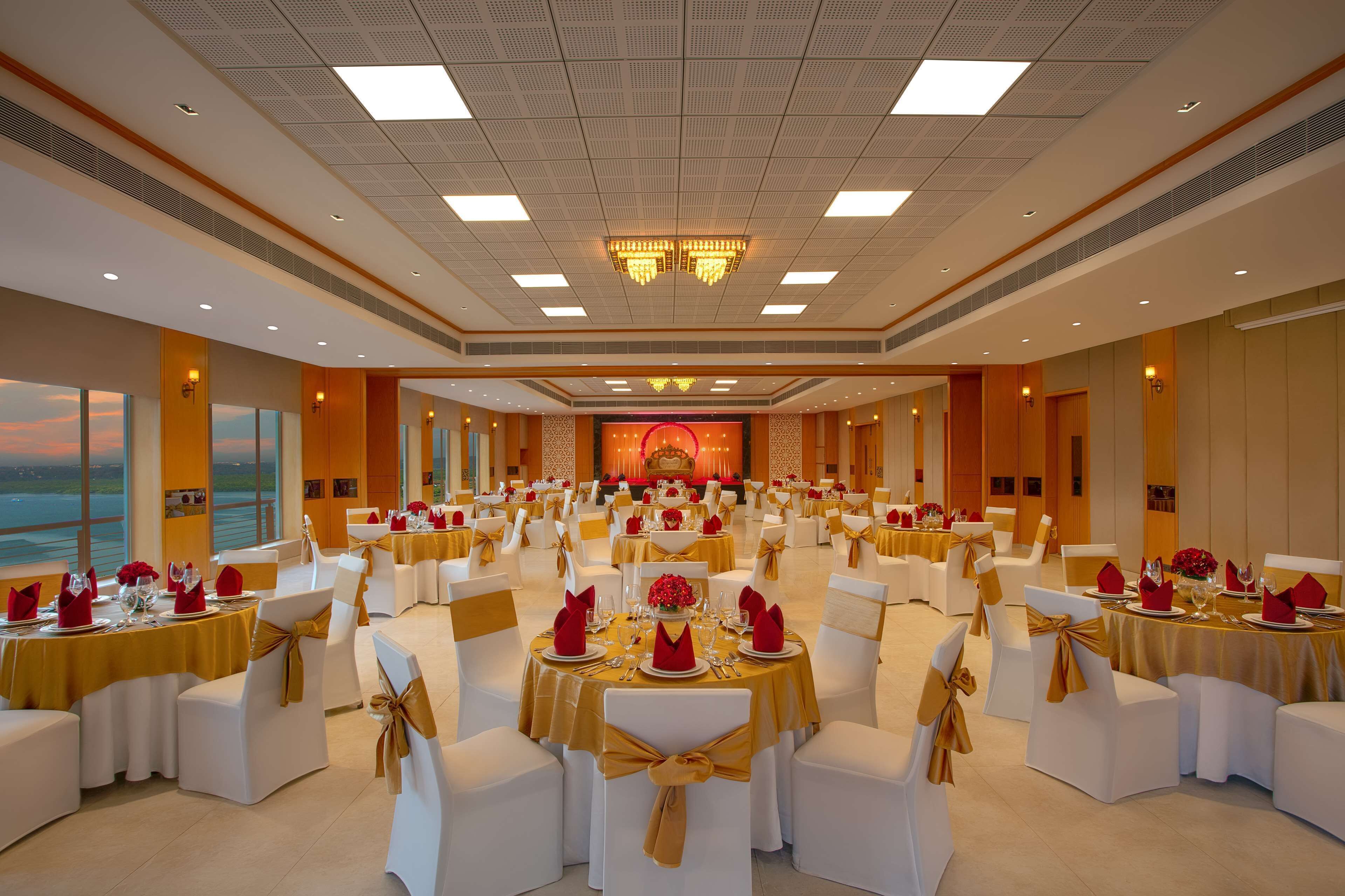 Een feestzaal met ronde tafels, witte stoelen en gouden accenten.