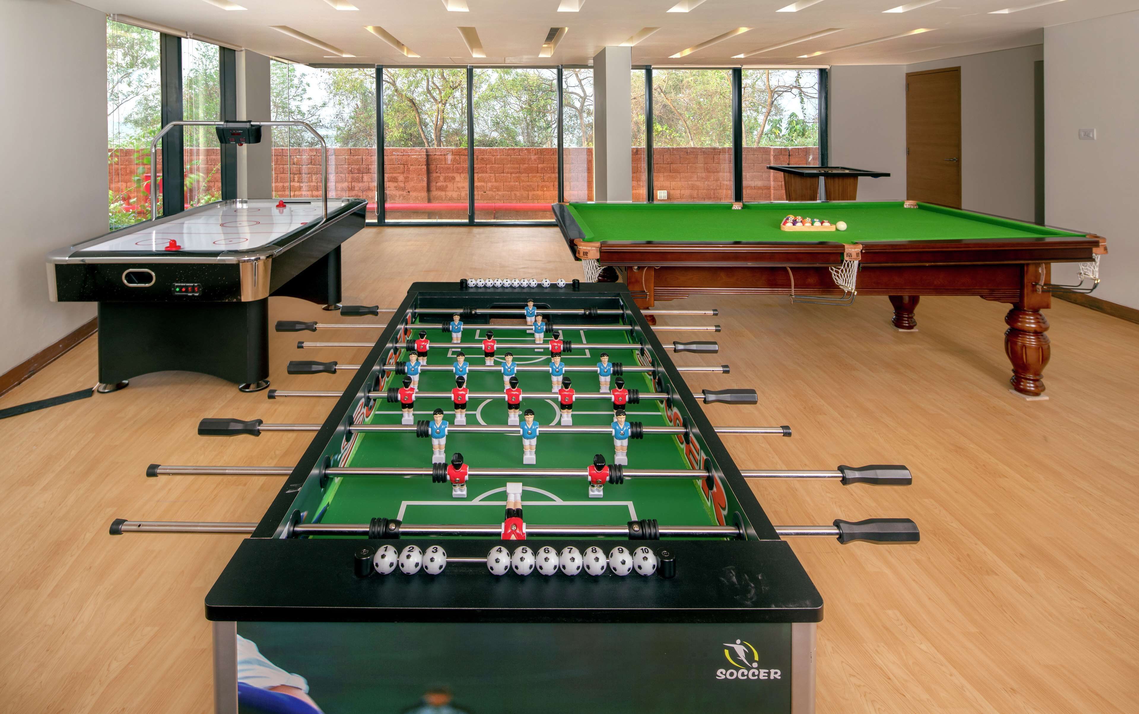 A room with a foosball table, a pool table, and a foosball table with a soccer theme.