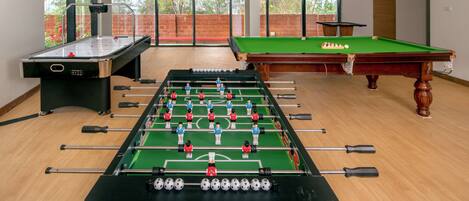 A room with a foosball table, a pool table, and a foosball table with a soccer theme.