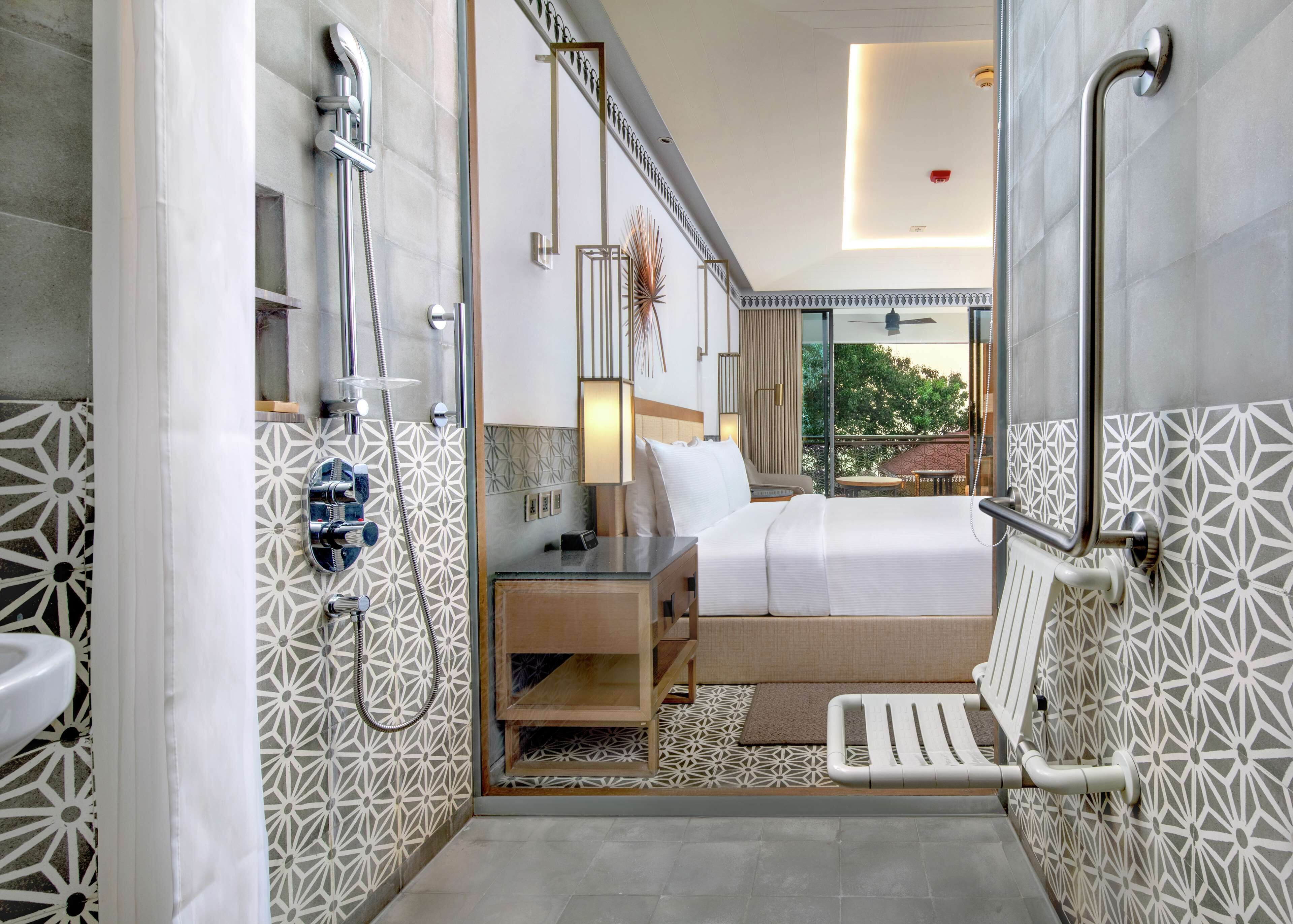 A modern hotel bathroom with a shower, toilet, and a bed with a view of the outdoors.