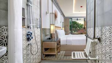 A modern hotel bathroom with a shower, toilet, and a bed with a view of the outdoors.