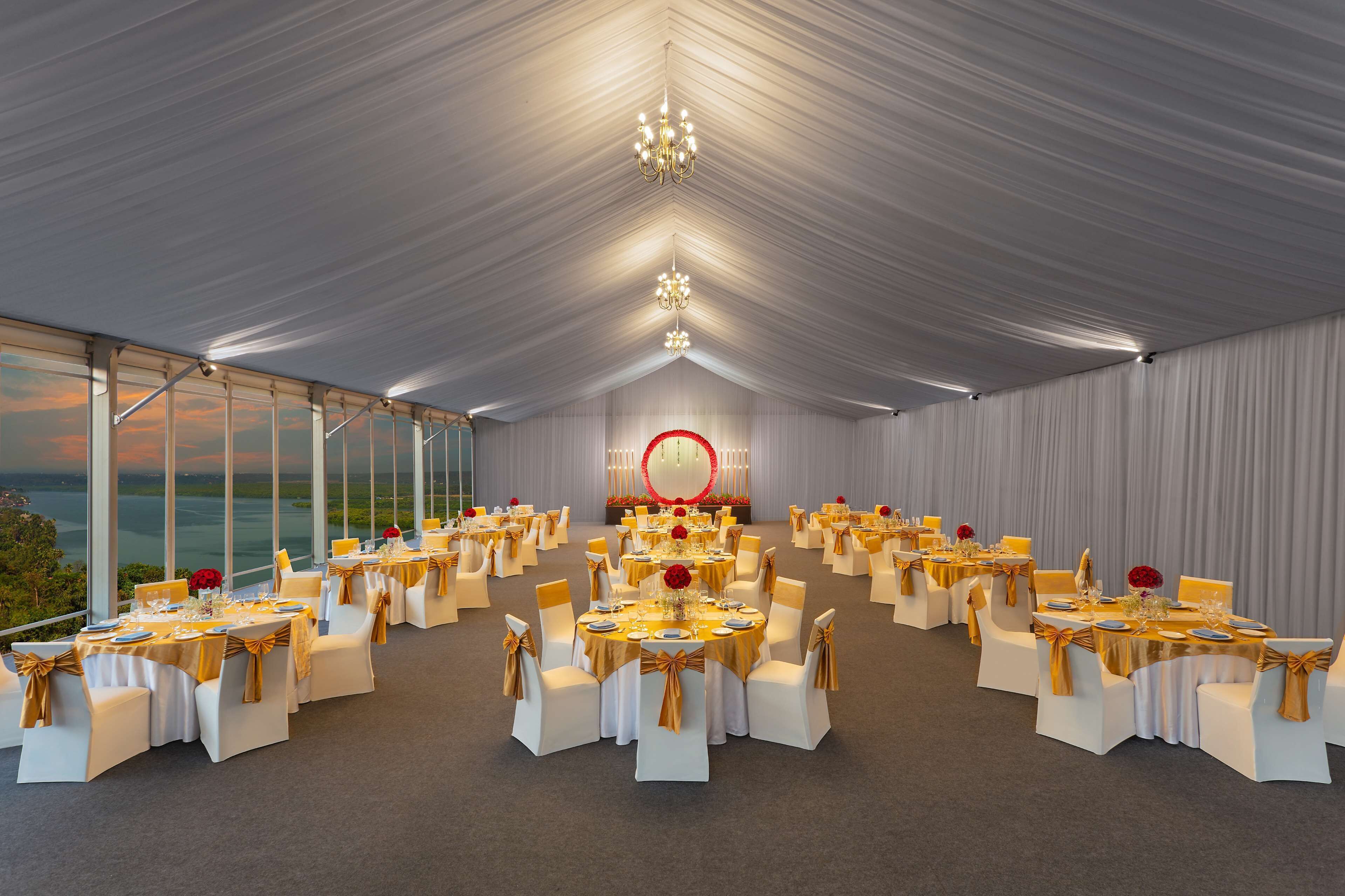 Un salón de banquetes con mesas redondas, sillas blancas y detalles dorados.