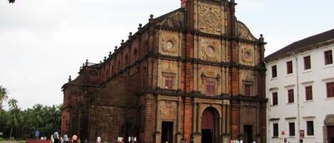 Un edificio histórico con un amplio arco central, una torre de reloj y un edificio blanco adyacente.