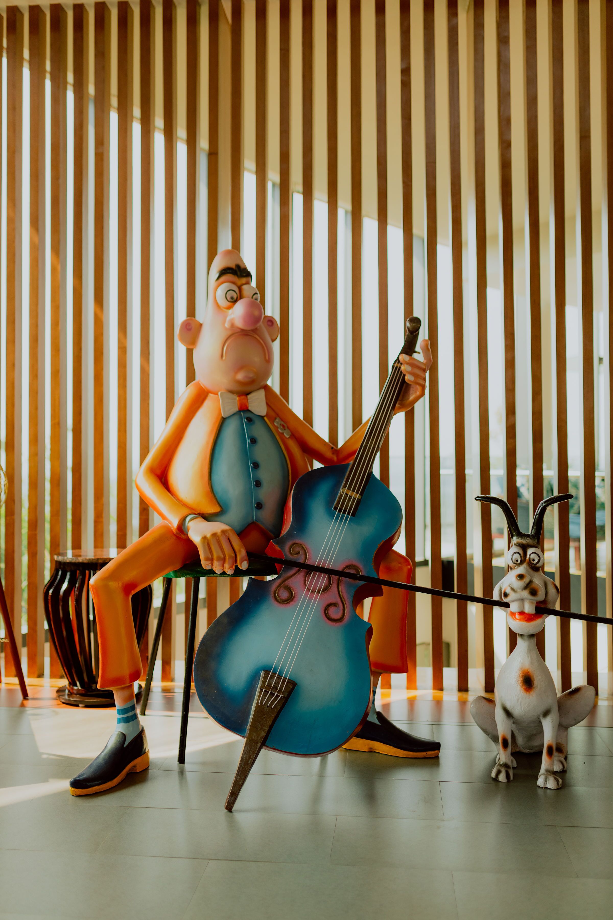 A cartoon character playing a cello in a room with vertical wooden slats.