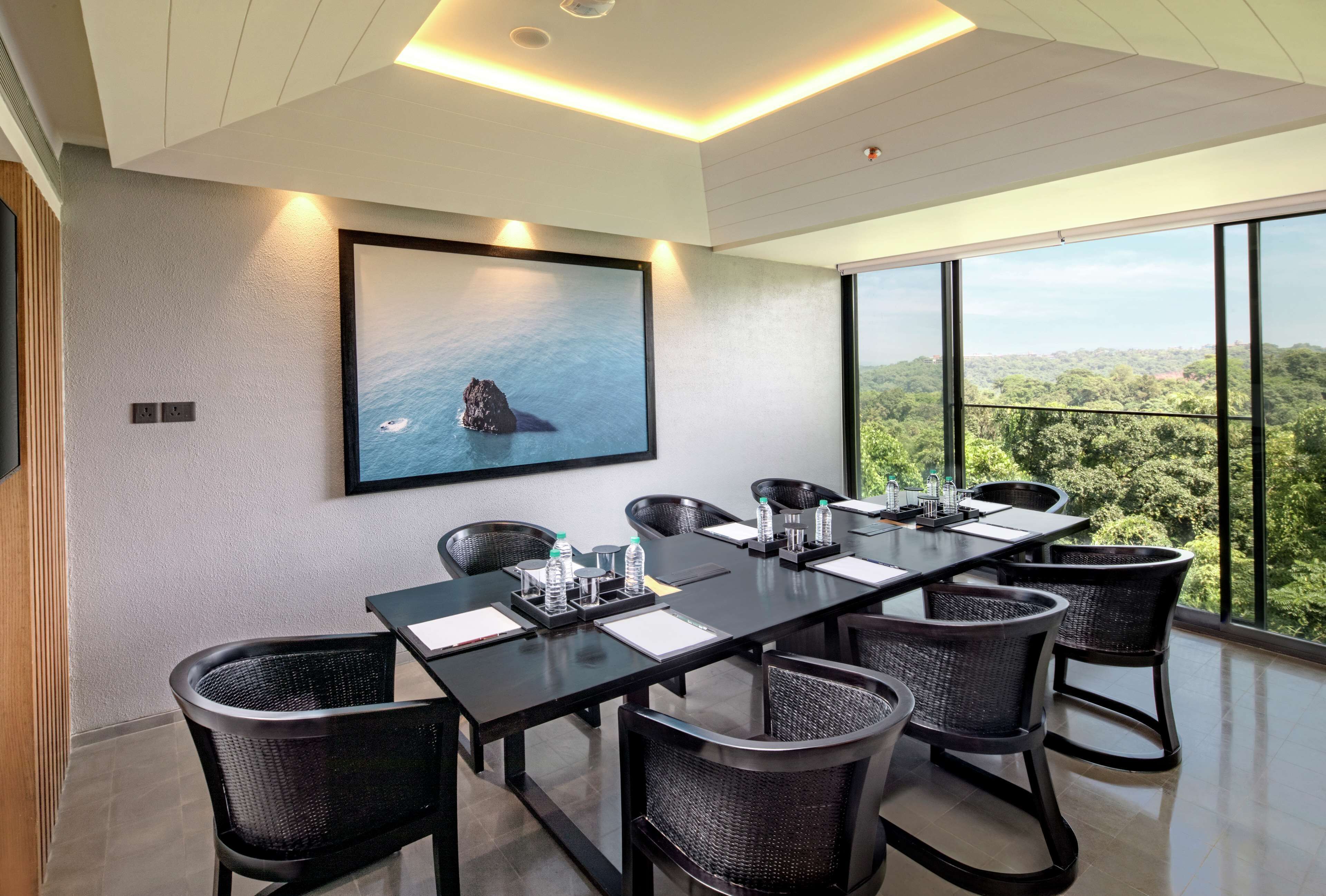 A modern conference room with a long table, black chairs, and a large painting of a rock in the sea.