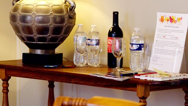 Ein Tisch mit Lampe, einer Weinflasche, Wasserflaschen und einem Bilderrahmen mit einem Bild von einer Scheune.