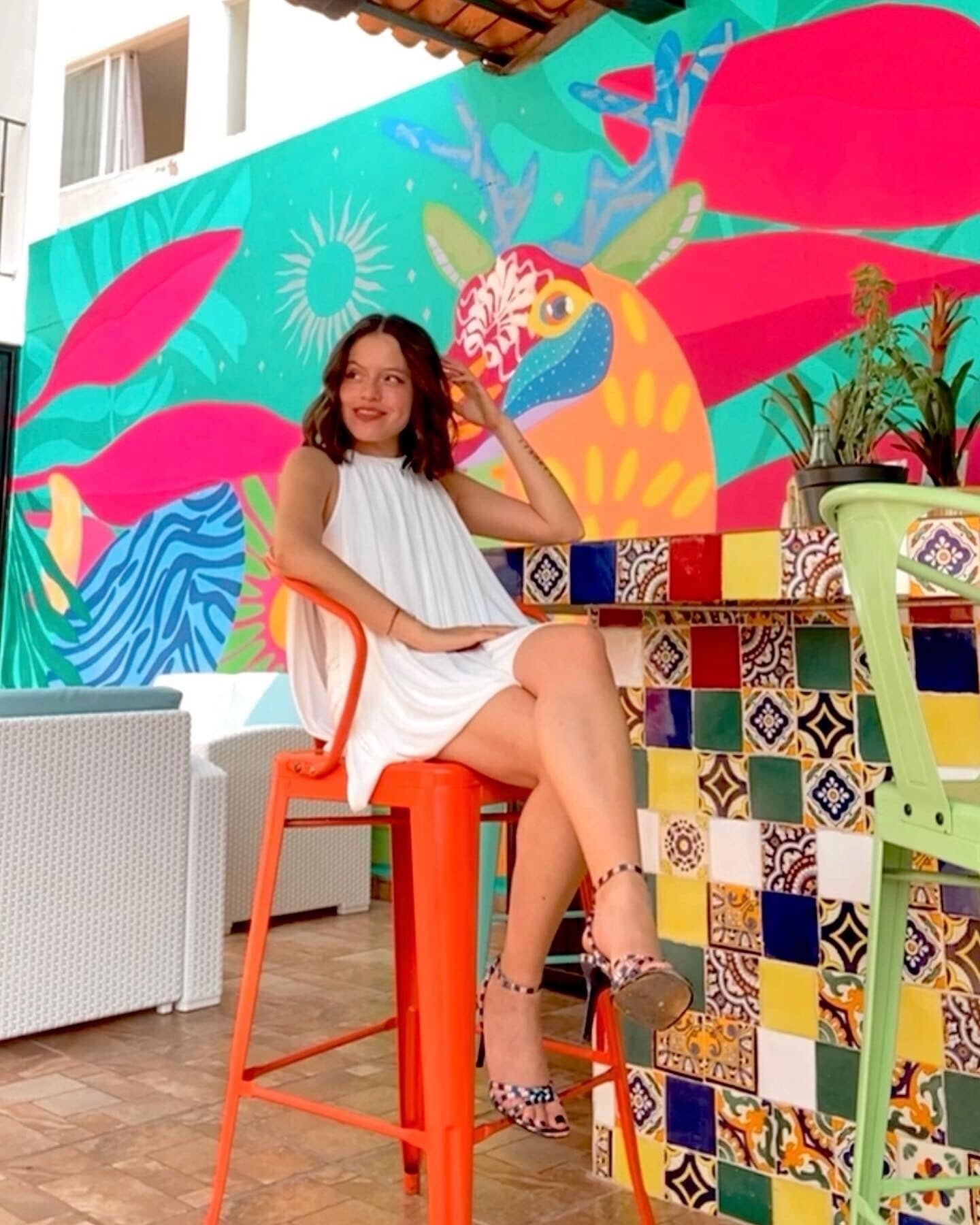 A person sitting on an orange chair at a table with a colorful tiled wall behind them.