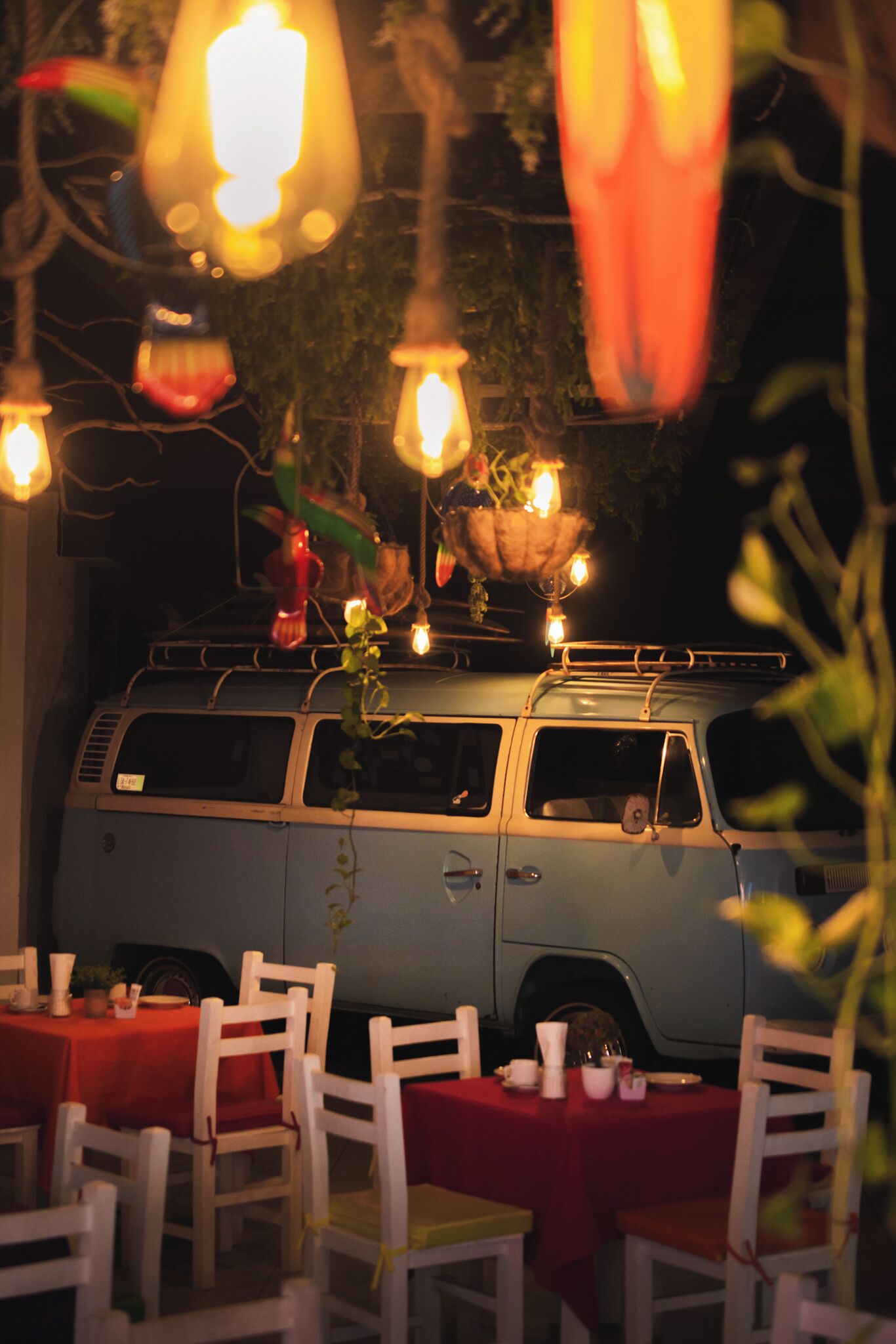 A van with a red tablecloth and white chairs set up in front of it.