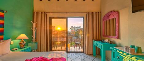 A hotel room with a bed, a desk, a dresser, and a balcony with a view of the city.