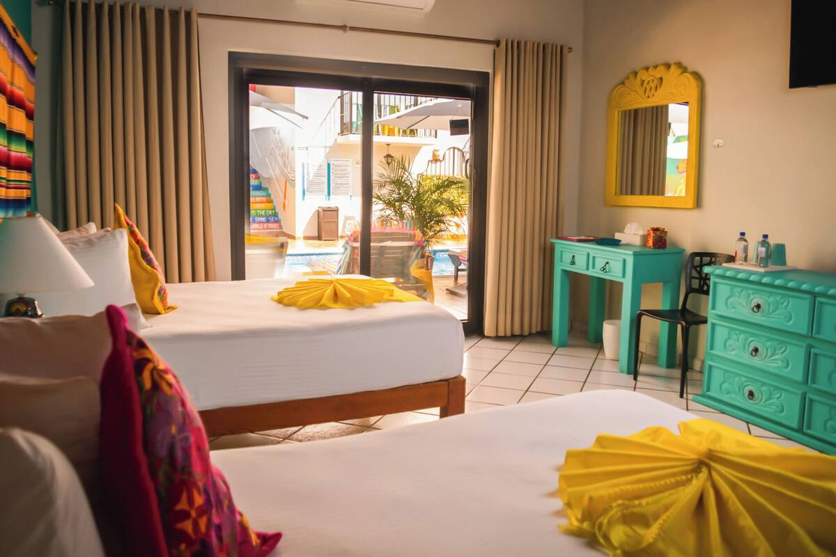 A hotel room with a bed, a desk, a chair, a mirror, and a view of the outside.