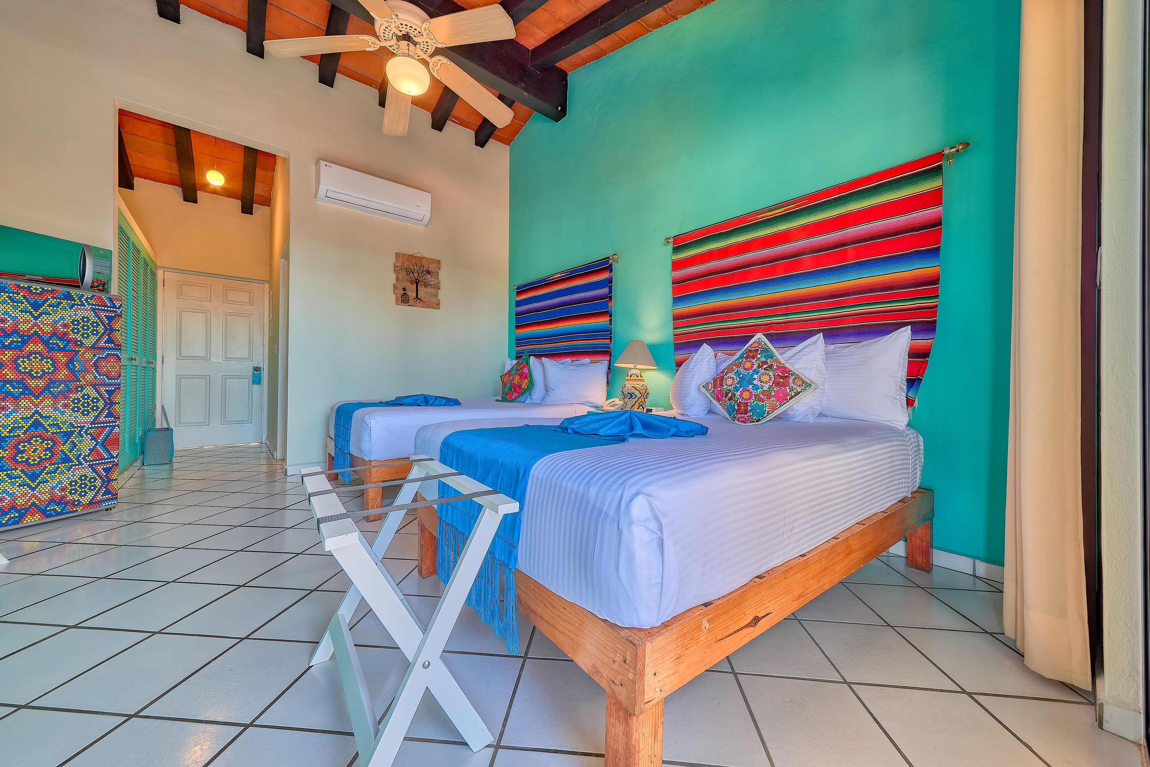 Una habitación con dos camas, un ventilador de techo y una pared colorida.