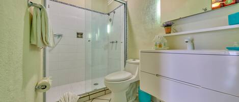 A bathroom with a glass-enclosed shower, a toilet, and a white vanity with drawers.