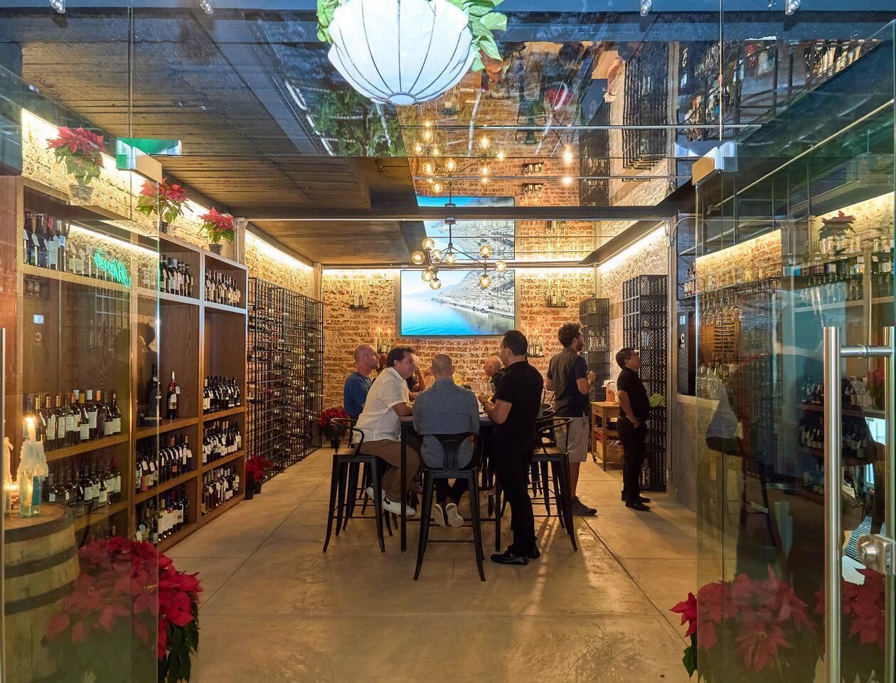 Une cave à vin avec des étagères en bois, un grand écran de télévision et un groupe de personnes réunies autour d’une table.