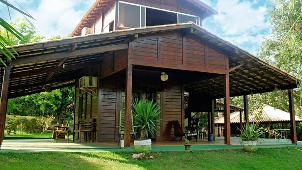 A wooden building with a covered patio area, large windows, and a view of the surrounding greenery. - Hotel Fazenda Rio Formoso (Bonito)