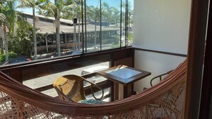 Un balcón con techo de madera, ventanas amplias, una hamaca y una mesa con sillas.