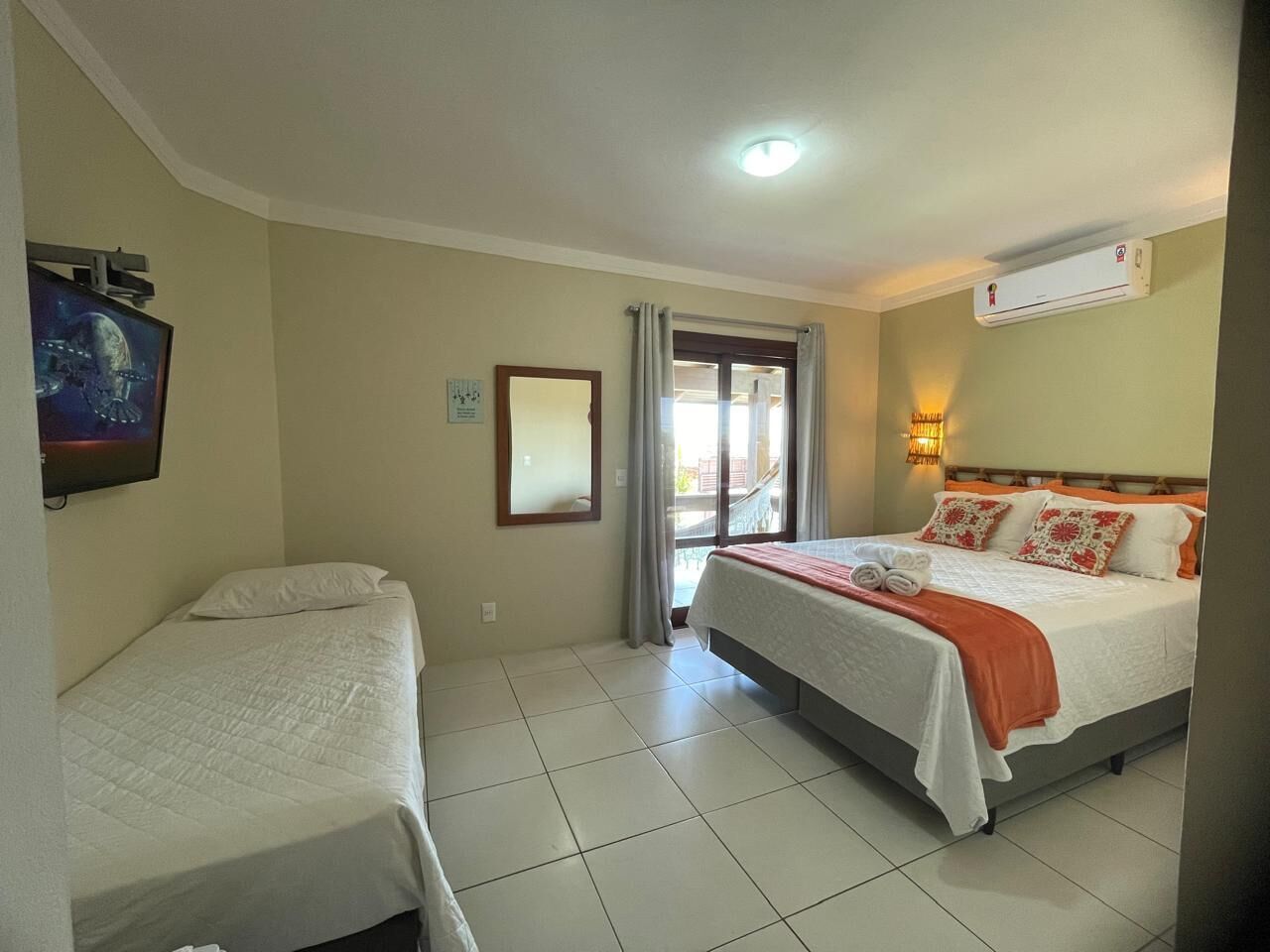 A hotel room with two beds, a television, a mirror, and an air conditioning unit.