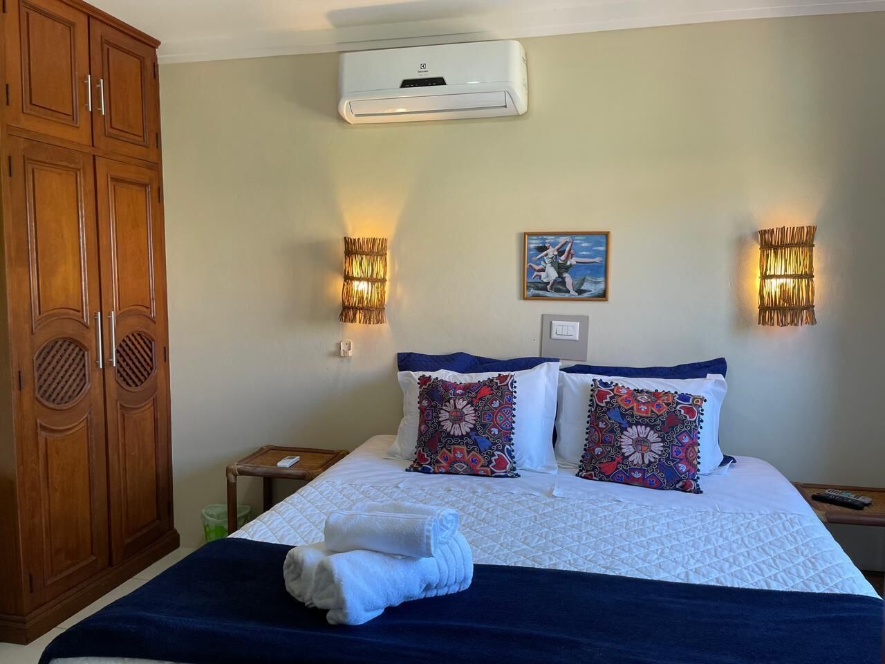 Una habitación de hotel con cama, dos apliques decorativos, un cuadro y un armario.