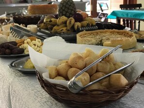 A buffet table with various food items including bread, fruits, and pastries. - Pousada Vivenda da Barra (Torres)