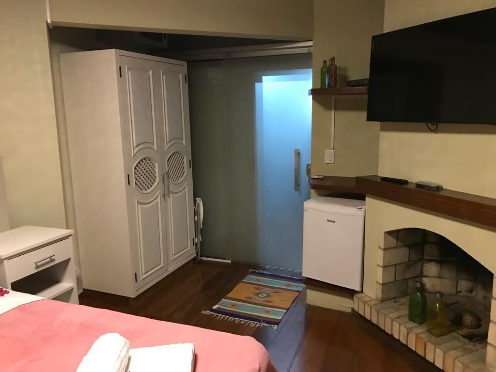 Un dormitorio con cama, armario, televisor, chimenea y un refrigerador pequeño.