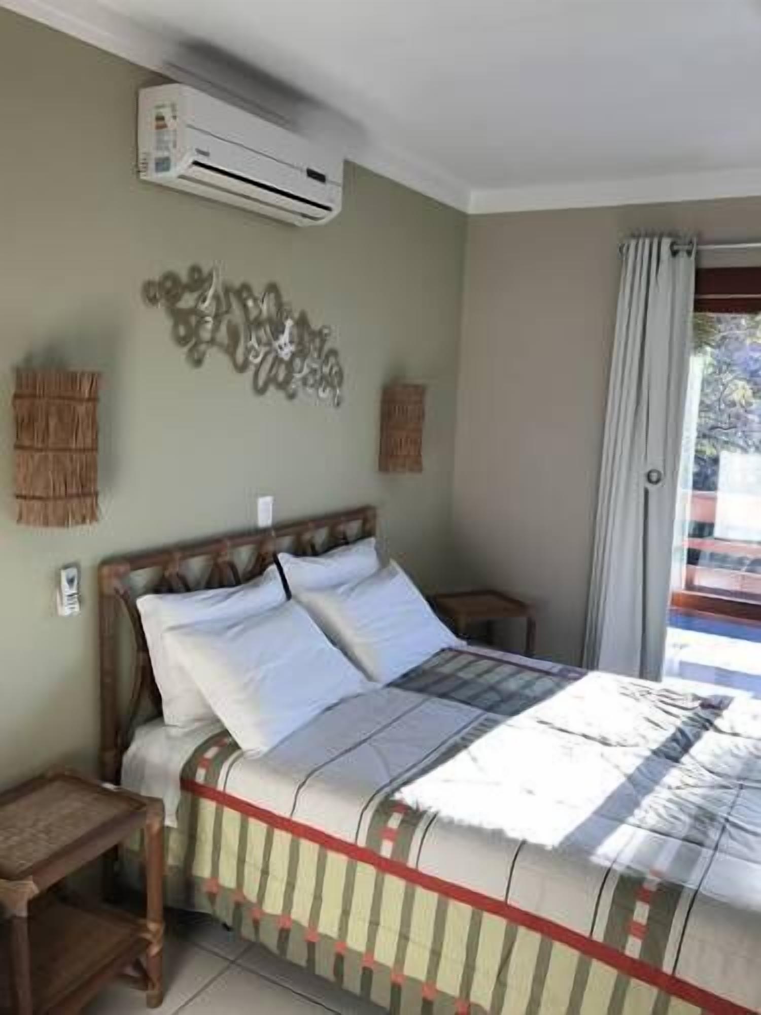 Une chambre à coucher comprenant un lit, une table de chevet en bois, un climatiseur fixé au mur et un élément décoratif mural.