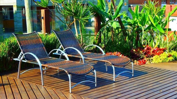 Dos sillones de descanso en una terraza de madera con un jardín tropical de fondo.
