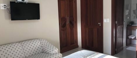 Un dormitorio con cama, sofá, televisor montado en la pared y puertas de madera.