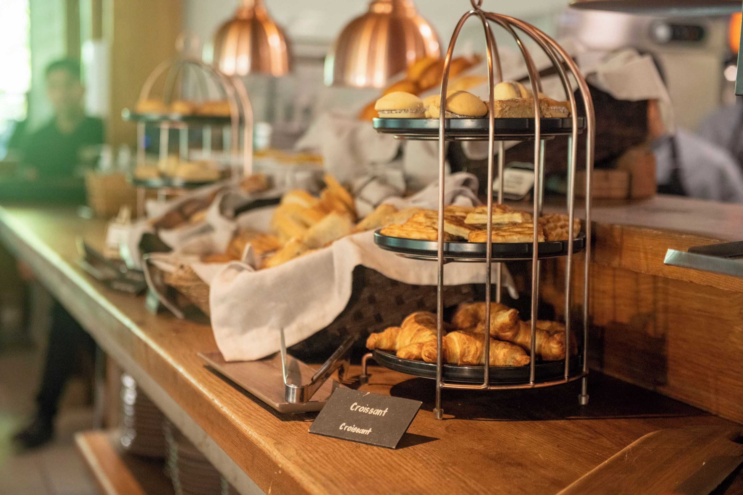 A buffet counter with multiple trays of pastries and bread, including croissants, arranged on a wooden counter.