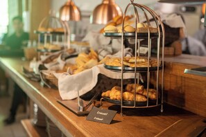 A buffet counter with multiple trays of pastries and bread, including croissants, arranged on a wooden counter. - Hotel Las Majadas (Pirque)