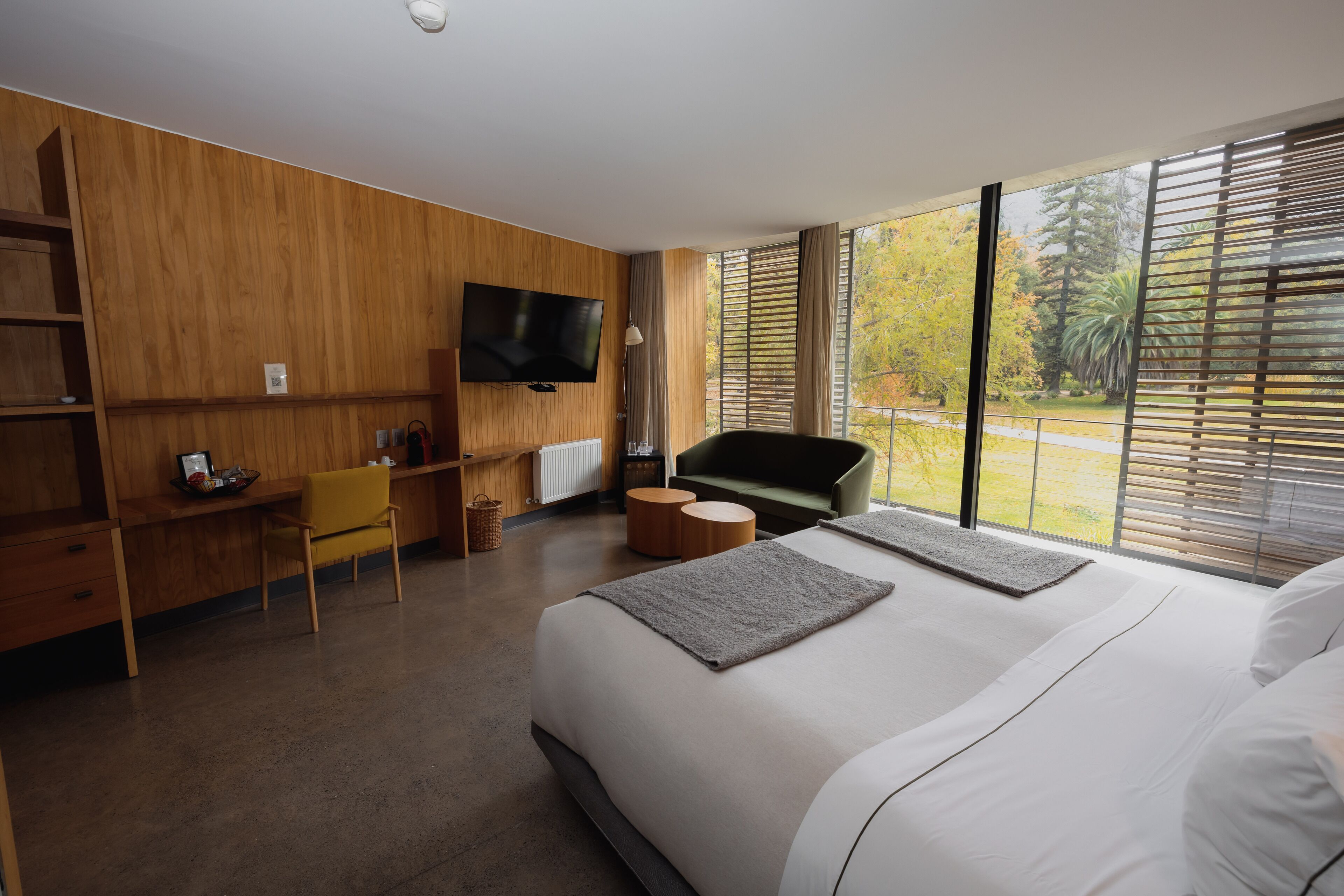 Habitación de hotel moderna con una cama grande, un escritorio con silla, televisión y vista a árboles por la ventana.