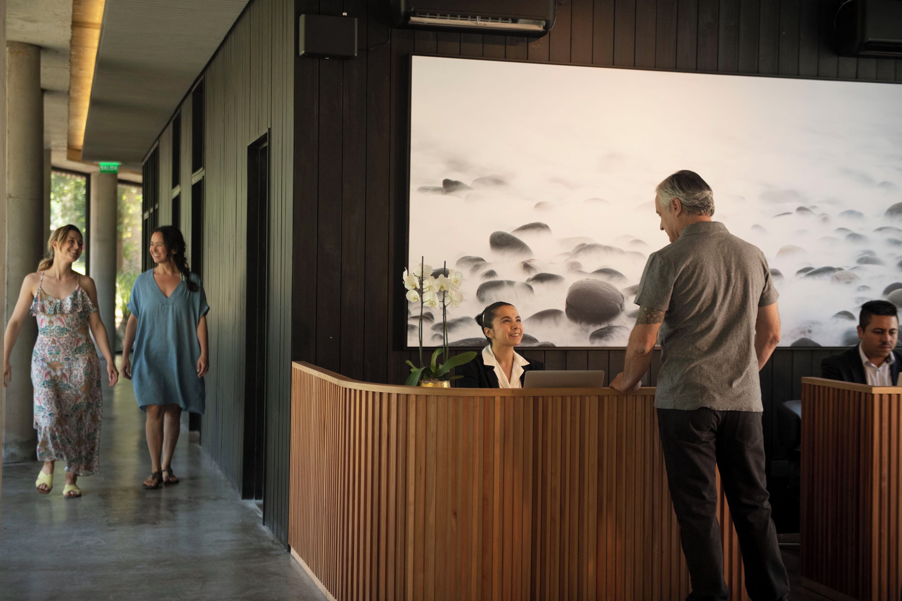 A reception area with a wooden reception desk, a large wall-mounted artwork depicting rocks and water, and a corridor with columns.