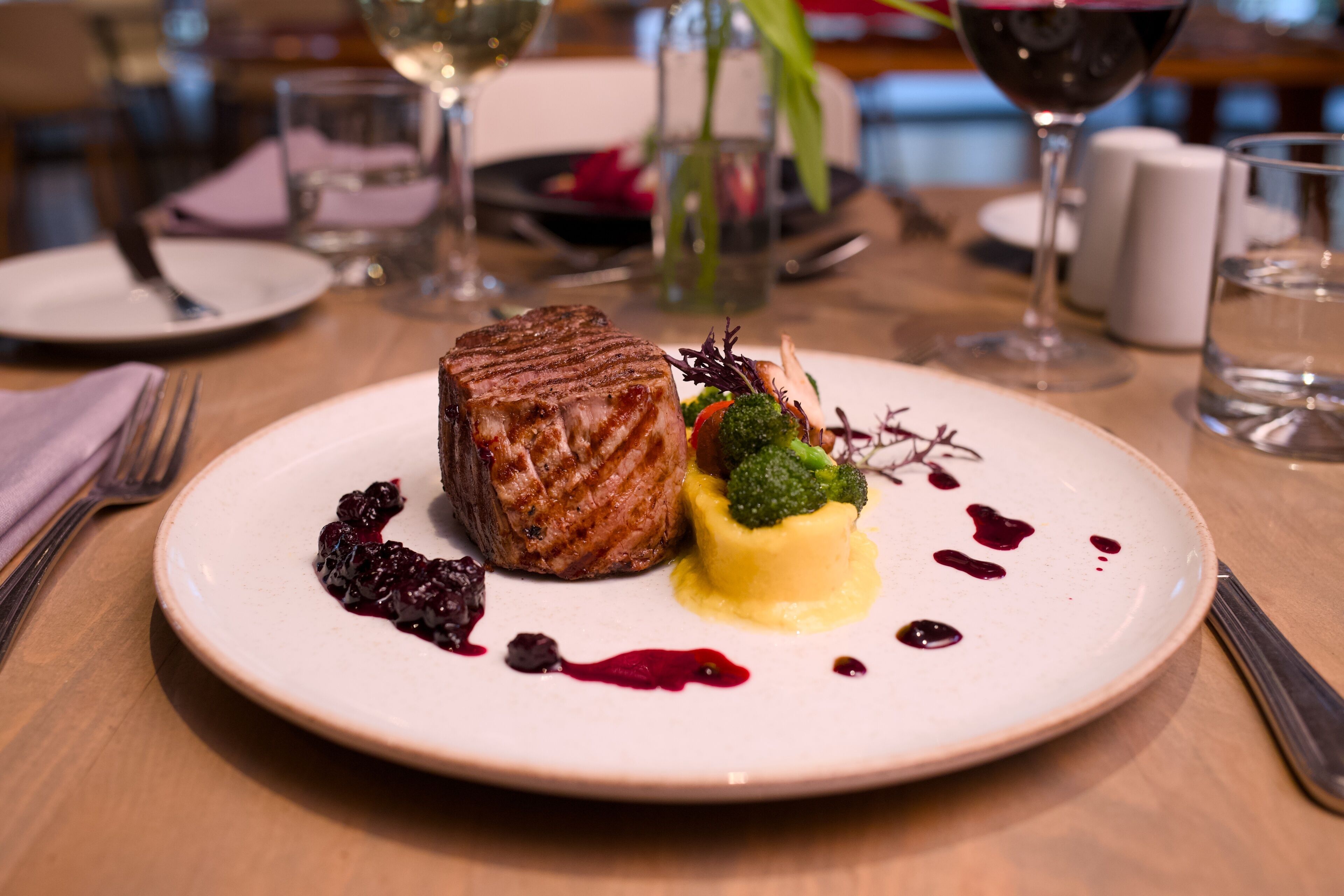 Ein Teller mit gegrilltem Steak, Brokkoli als Beilage und einer gelben Soße, dazu ein Glas Rotwein.