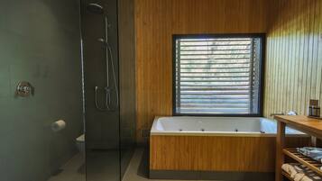 Un baño moderno con ducha de vidrio, una bañera independiente y una ventana con persianas.
