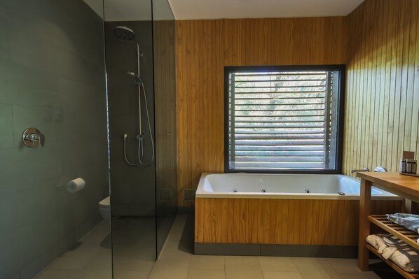 A modern bathroom with a glass-enclosed shower, a freestanding bathtub, and a window with blinds.