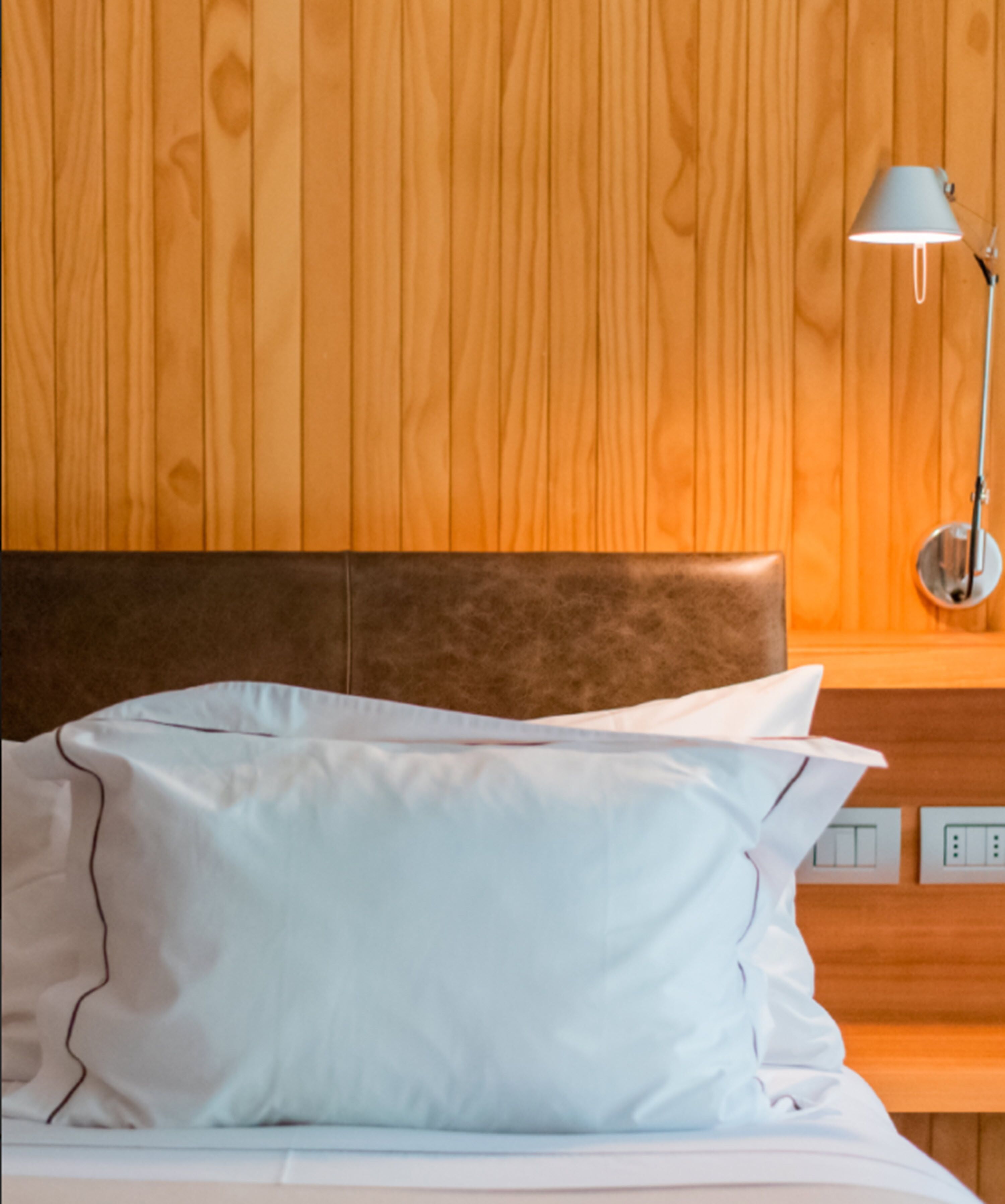 Una cama con sábanas blancas y un cabecero frente a una pared de madera.