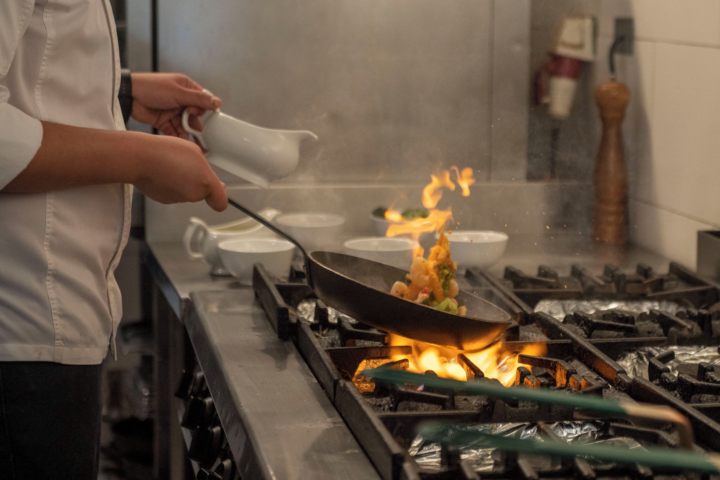 Un chef cocina con un wok en una hornilla, rodeado de varios cuencos.