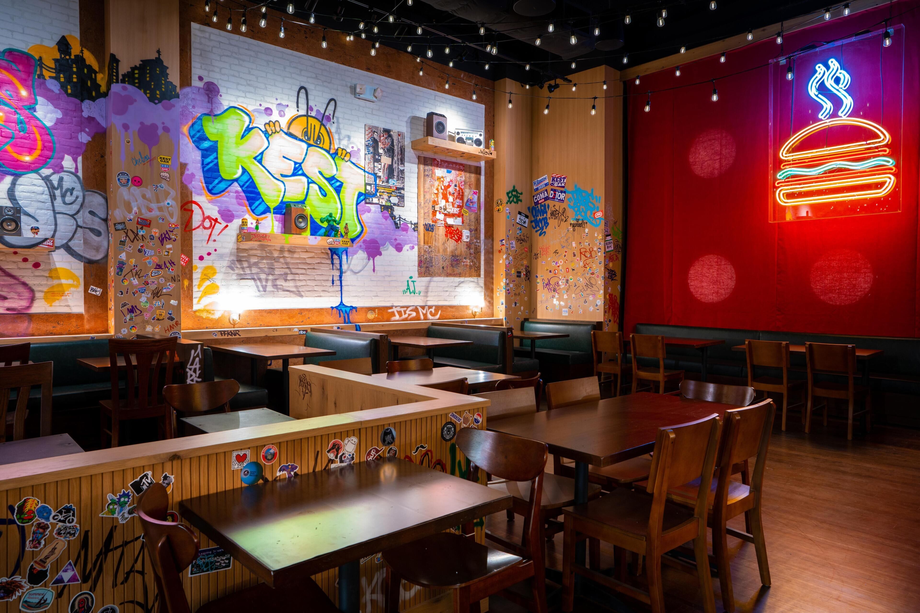 A restaurant interior with graffiti art, neon signs, wooden tables, and booths.