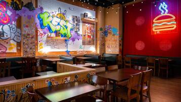 A restaurant interior with graffiti art, neon signs, wooden tables, and booths.