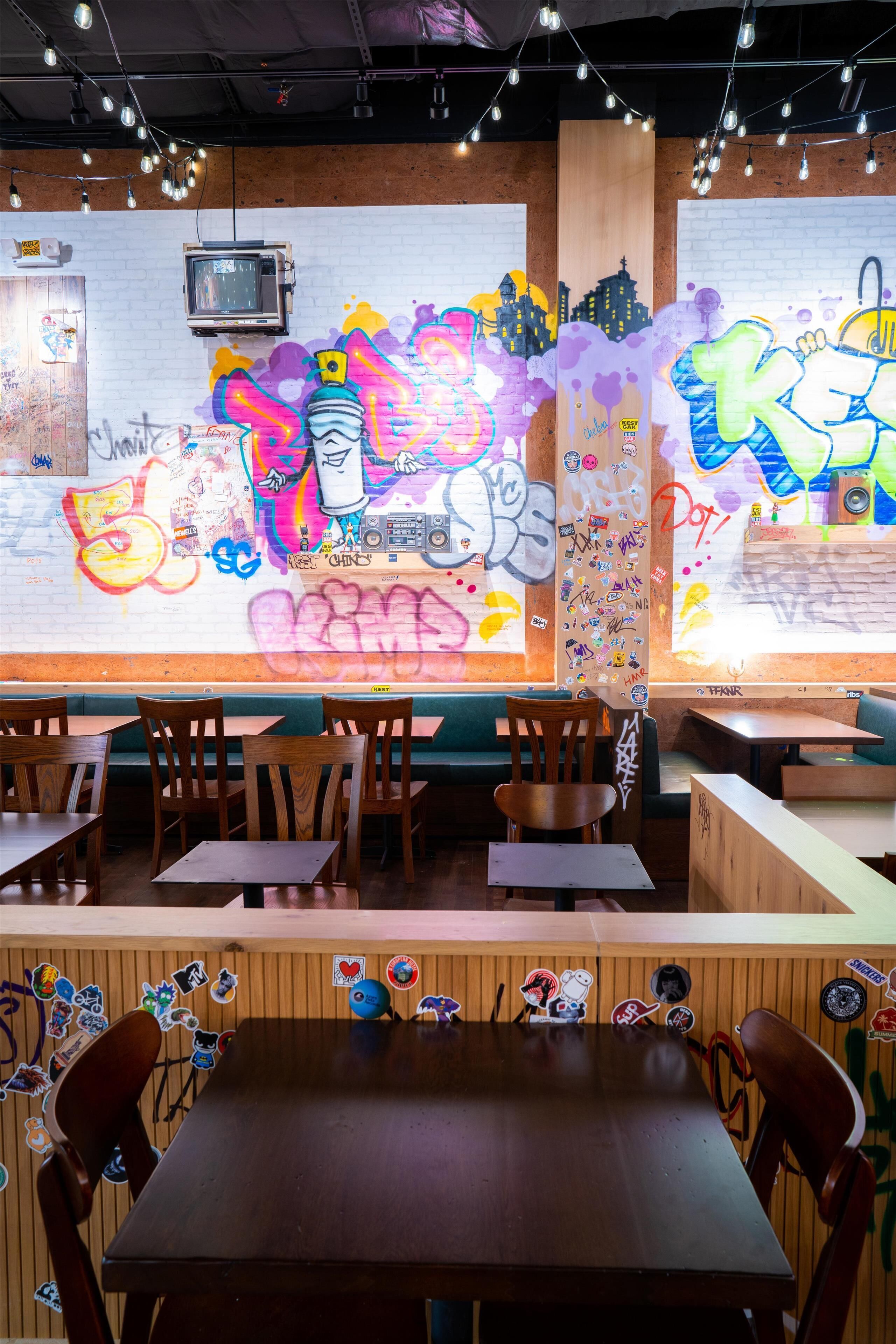 A restaurant with graffiti art on the walls, wooden tables, and chairs.