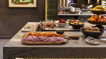 A buffet table with various food items, including fruits, vegetables, and a bowl of salmon.