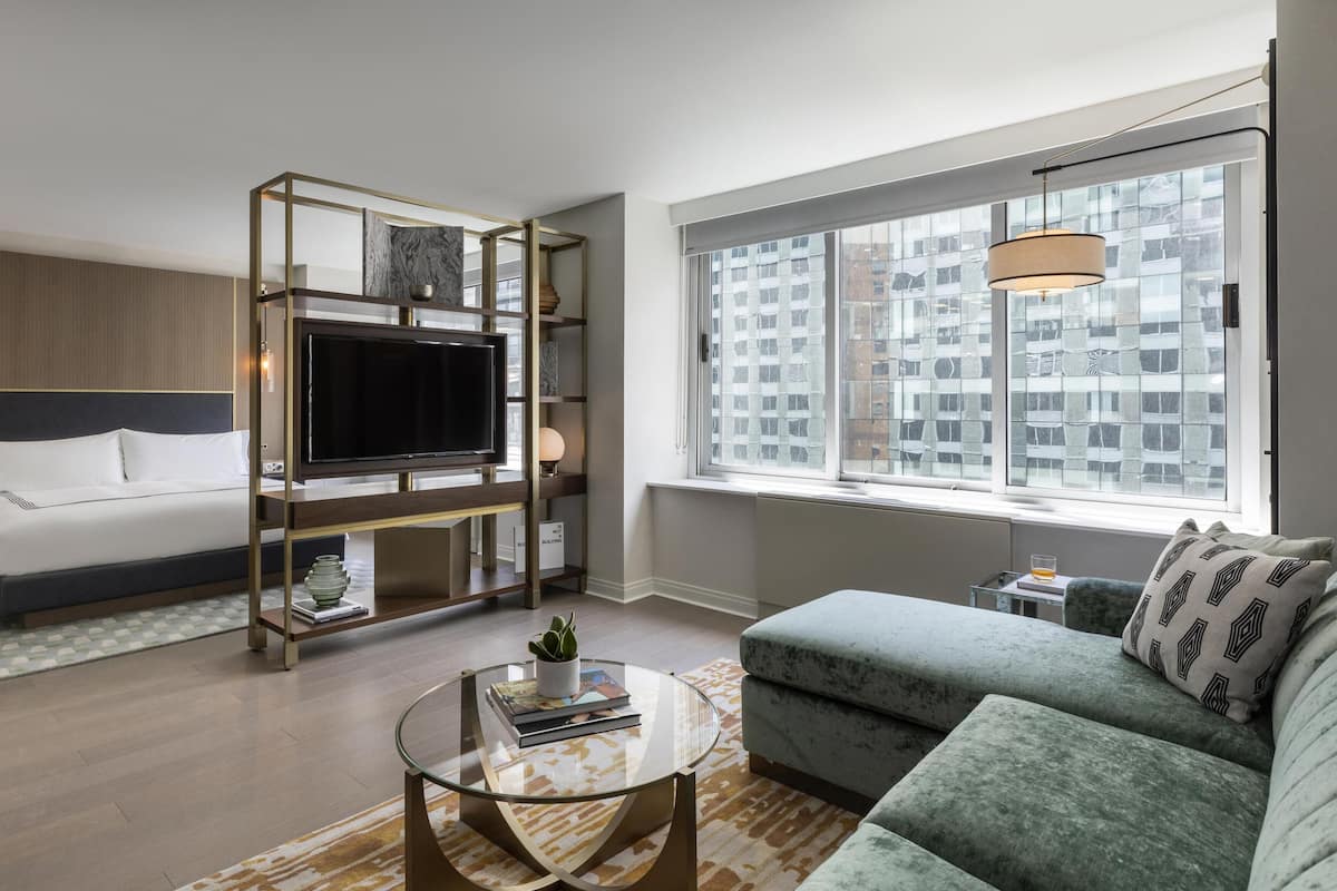 Quarto de hotel moderno com uma cama, televisão, sofá e uma grande janela.